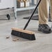 A person sweeping the floor with a Lavex wood push broom head.