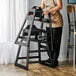 A woman standing in front of a black wooden high chair.