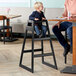 A young boy sitting in a Lancaster Table & Seating black wooden high chair.