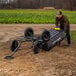 A man in a brown coat pushing a Gorilla heavy-duty poly yard dump cart on dirt.