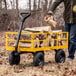 A yellow heavy-duty steel utility cart loaded with firewood being used outdoors.
