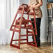 A woman standing next to an unassembled Lancaster Table & Seating wooden high chair with mahogany finish.