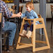 A man sitting at a table with a child sitting in a Lancaster Table & Seating wooden high chair.