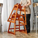 A woman standing next to a Lancaster Table & Seating wooden high chair with a walnut finish.