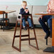 A young boy sitting in a Lancaster Table & Seating high chair drinking from a box.