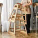 A woman standing next to an unassembled Lancaster Table & Seating wooden high chair.