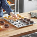 A person picking up a tray of cupcakes from a Thunder Group aluminum muffin pan.