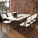 A white Lifetime folding table with a laptop on it surrounded by white chairs.