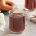 A glass mug filled with brown Crown Beverages Organic Donut Shop coffee next to a cup of coffee with steam and donuts.