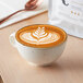 A cup of Arrosto decaf coffee with a leaf design in the foam on a table.