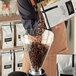 A man pouring Arrosto Colombian Supremo whole bean coffee into a grinder on a table in a coffee shop.