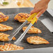 A person using Fourt&#233; yellow stainless steel tongs to grill chicken.