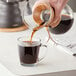 A person pouring Arrosto Brazil Santos Especial coffee into a glass cup.