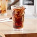 A glass of brown liquid with ice on a table.