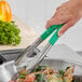 A person using Fourt&#233; green stainless steel scalloped tongs to serve food.