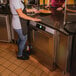 A woman standing in a commercial kitchen with a Hobart undercounter dishwasher on a counter.