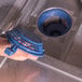 A person holding a blue filter component inside a commercial undercounter dishwasher.