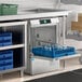A commercial high temperature undercounter dishwasher with a blue rack of glassware loaded inside.