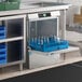A commercial undercounter dishwasher with a blue rack holding glassware, installed beneath a stainless steel countertop.