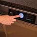 A person pressing the start button on a Hobart Advansys high temperature undercounter dishwasher.