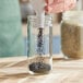 A person pouring black seeds from a glass jar.