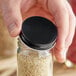 A person holding a jar with a 48/400 Black Metal Lid filled with sesame seeds.