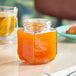 A 9 oz. oval hex jar of orange marmalade on a table in a breakfast diner.