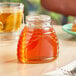 A glass hive jar of honey on a table next to a cup of tea.