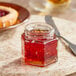 A 4 oz. hex glass jar of jam on a table next to a knife.