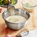 A person holding a measuring cup with white powder stirring it into a bowl of food.