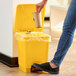 A woman throwing a coffee cup into a yellow Lavex step-on trash can.