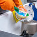 A pair of orange latex rubber gloves being used to wash dishes in a sink.