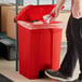 A man putting a trash bag into a Lavex red rectangular step-on trash can.