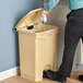 A person cleaning a Lavex tan rectangular step-on trash can.