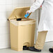 A person in a white lab coat putting a blue glove in a Lavex rectangular step-on trash can.