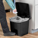 A hand putting a plastic bag into a black Lavex rectangular step-on trash can.