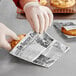 A person in gloves using a Choice newsprint deli wrap to hold a cookie on a bakery counter.