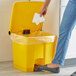 A woman using a Lavex yellow rectangular step-on trash can to throw away a tissue.