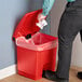 A person's hand throws a white paper into a red Lavex rectangular step-on trash can.