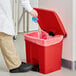 A person in a lab coat putting a glove into a red Lavex rectangular step-on trash can.