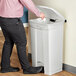 A person in a pink shirt using a Lavex rectangular step-on trash can to throw paper away.