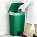 A man in a lab coat using a Lavex green rectangular step-on trash can to throw away gloves.