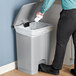 A man's hand putting a plastic bag into a Lavex rectangular step-on trash can.