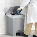 A person in a white coat putting a blue glove in a Lavex step-on trash can.