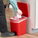 A person throwing a paper into a red Lavex rectangular step-on trash can.