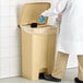 A person in a white lab coat stepping on a Lavex rectangular step-on trash can to throw away a glove.