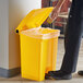 A person putting a paper into a yellow Lavex step-on trash can.