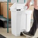 A person using a Lavex white rectangular step-on trash can.