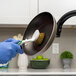 A person in blue gloves using a Libman Polypropylene Pot Scrub Brush to clean a pan.