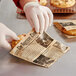 A person in gloves using a Choice kraft newsprint double open bag to wrap a cookie on a bakery counter.